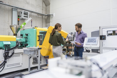 Geschäftsmann und Frau bei einer Besprechung vor Industrierobotern in einem Hightech-Unternehmen - DIGF05228