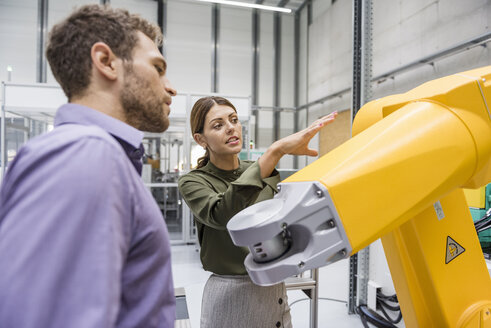 Geschäftsmann und Frau bei einer Besprechung vor Industrierobotern in einem Hightech-Unternehmen - DIGF05229