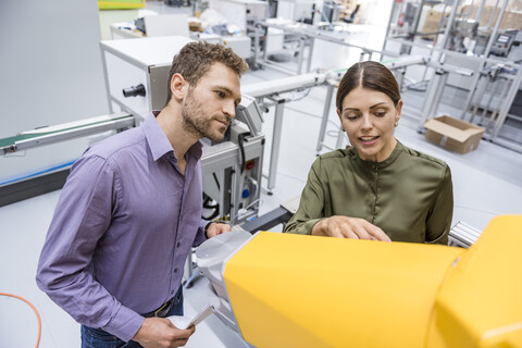 Geschäftsmann und Frau bei einer Besprechung vor Industrierobotern in einem Hightech-Unternehmen, lizenzfreies Stockfoto