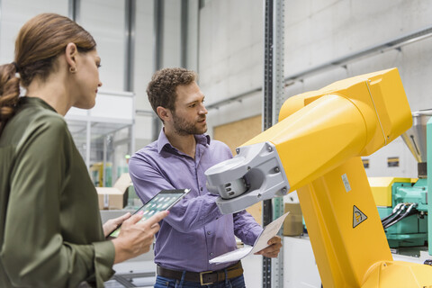 Businessman and woman having a meeting in front of industrial robots in a high tech company stock photo