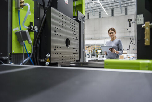 Geschäftsfrau in einem Hightech-Unternehmen, die Produktionsmaschinen mit einem digitalen Tablet kontrolliert - DIGF05242