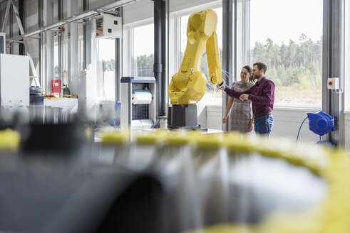 Businessman and woman having a meeting in front of industrial robots in a high tech company - DIGF05254