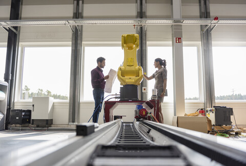 Geschäftsmann und Frau bei einer Besprechung vor Industrierobotern in einem Hightech-Unternehmen, lizenzfreies Stockfoto