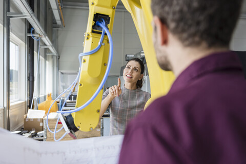 Businessman and woman having a meeting in front of industrial robots in a high tech company stock photo