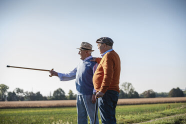 Zwei alte Freunde stehen auf den Feldern und zeigen mit dem Spazierstock auf etwas - UUF15455