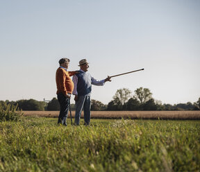 Zwei alte Freunde stehen auf den Feldern und zeigen mit dem Spazierstock auf etwas - UUF15456