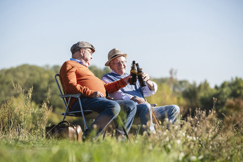 Two old friends sitting in the fields, drinking beer, talking about old times - UUF15478