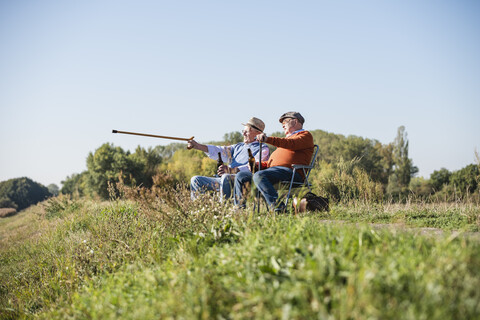 Zwei alte Freunde sitzen auf den Feldern, trinken Bier und zeigen mit dem Spazierstock auf etwas, lizenzfreies Stockfoto