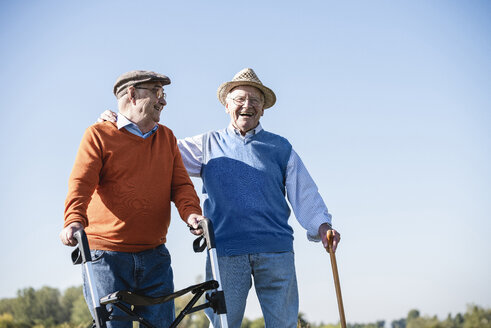 Old friends taking a stroll in the fields with walking stick and wheeled walker, talking about old times - UUF15492