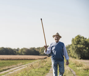 Älterer Mann, der in den Feldern spazieren geht und mit seinem Gehstock grüßt - UUF15498