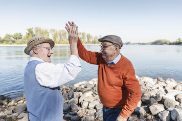 Two laughing old friends high-fiving at a lake - UUF15514