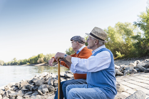 Zwei alte Freunde sitzen auf einem Baumstamm und beobachten den Fluss, lizenzfreies Stockfoto