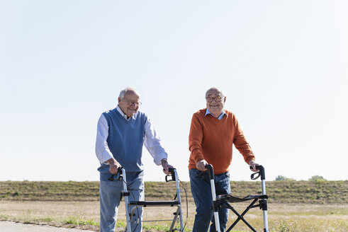 Two old friends walking on a country road, using wheeled walkers - UUF15526