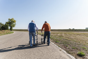 Zwei alte Freunde, die auf einer Landstraße spazieren gehen, mit Rollatoren - UUF15528