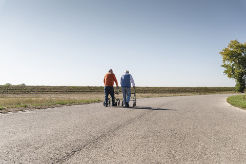 Zwei alte Freunde, die auf einer Landstraße spazieren gehen, mit Rollatoren, lizenzfreies Stockfoto