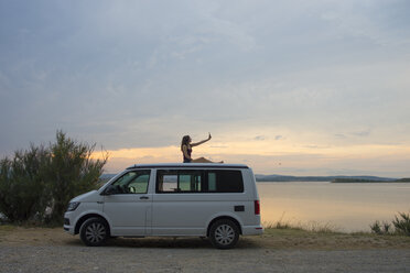 Woman on top of the van making a selfie at sunset on the lake - SKCF00538