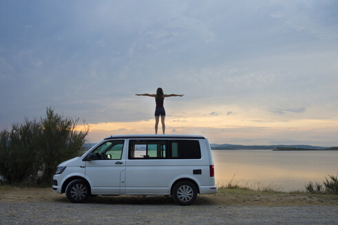 Frau auf dem Dach des Lieferwagens stehend, der bei Sonnenuntergang auf dem See ruht - SKCF00539