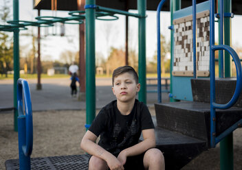 Trauriger Junge, der auf dem Spielplatz sitzt und wegschaut - CAVF49969