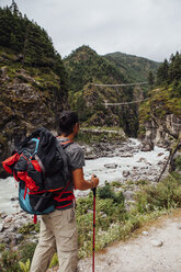Rear view of male hiker with backpack standing by river against cloudy sky at Sagarmatha National Park - CAVF49978