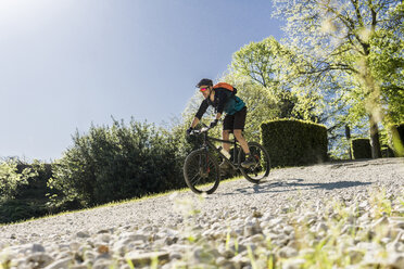 Surface level shot of young man riding mountain bike at park during sunny day - CAVF49984