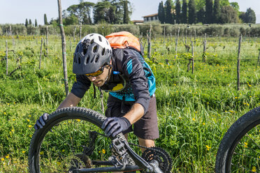 Junger Mann untersucht den Reifen eines Mountainbikes auf einem Feld - CAVF49988