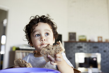 Close-up of cute thoughtful baby boy holding breads while looking away at home - CAVF50009