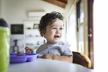 Nahaufnahme eines niedlichen, fröhlichen kleinen Jungen, der Brote hält, während er zu Hause wegschaut - CAVF50013