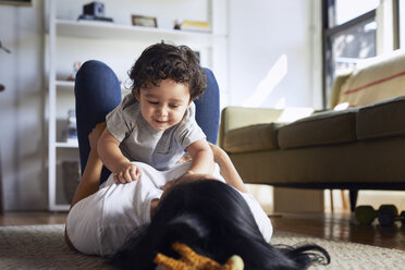 Mother playing with son while lying on carpet at home - CAVF50015