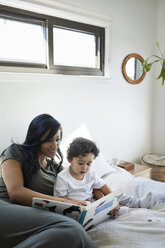 Mutter und Sohn betrachten ein Bilderbuch, während sie sich zu Hause auf dem Bett ausruhen - CAVF50016
