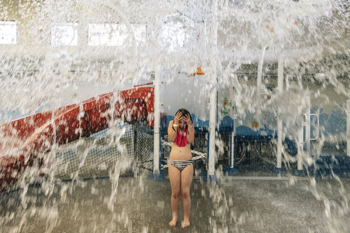 Mädchen steht in voller Länge unter spritzendem Wasser im Park - CAVF50021