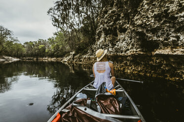 Rear view of young woman wearing hat while canoeing in lake at forest - CAVF50035