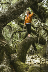 Junge Frau steht auf einem moosbewachsenen Ast im Regenwald - CAVF50041