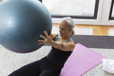 Ältere Frau, die einen Fitnessball hält, während sie zu Hause trainiert - CAVF50058