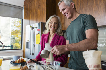 Mann bereitet Essen zu, während er neben einer lächelnden Frau in der Küche zu Hause steht - CAVF50059