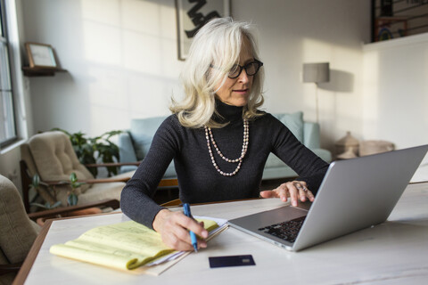 Ernste ältere Frau, die einen Laptop benutzt, während sie zu Hause Rechnungen bezahlt, lizenzfreies Stockfoto