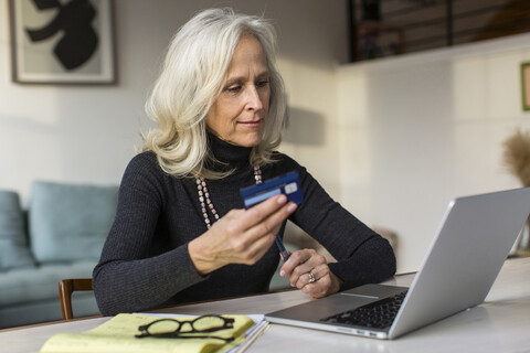 Ältere Frau benutzt Laptop beim Bezahlen von Rechnungen zu Hause, lizenzfreies Stockfoto