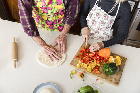 Mittelteil einer Frau, die eine Paprika schneidet, während ein Mann Pizzateig in der Küche zu Hause herstellt - CAVF50080