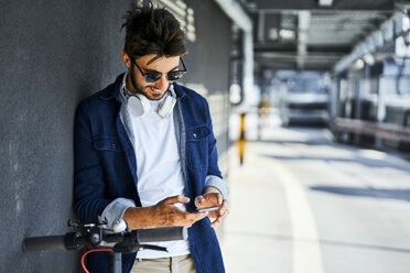 Smiling man with electric scooter using cell phone - BSZF00766