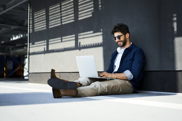 Relaxed young man sitting on the ground using laptop - BSZF00772