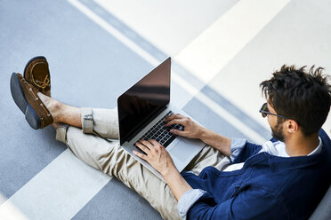 Young man sitting on the ground using laptop - BSZF00774