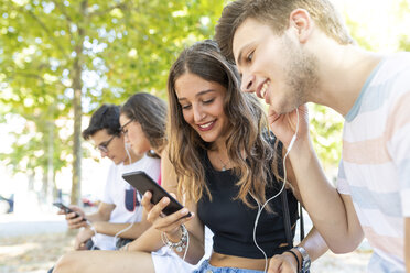 Group of friends at a park having fun together and listening to music on cell phones - WPEF00925