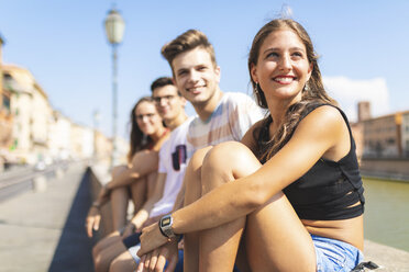 Italy, Pisa, group of four happy friends sitting on a wall along Arno river - WPEF00940