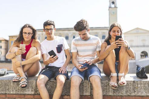 Italien, Pisa, Gruppe von vier Freunden, die zusammen auf einer Mauer sitzen und Handys benutzen - WPEF00942