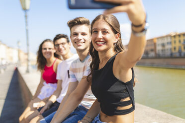Italy, Pisa, group of four happy friends sitting on a wall along Arno river taking a selfie - WPEF00943