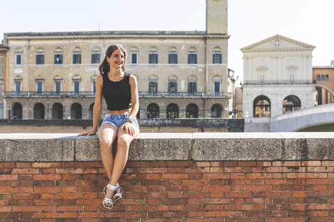 Italien, Pisa, junge Frau sitzt auf einer Mauer in der Stadt, lizenzfreies Stockfoto