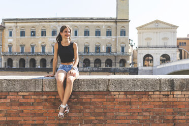 Italien, Pisa, junge Frau sitzt auf einer Mauer in der Stadt - WPEF00944