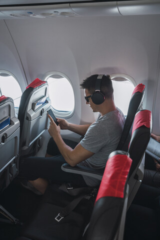 Mann im Flugzeug, mit Smartphone und Kopfhörern, lizenzfreies Stockfoto