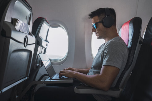 Mann im Flugzeug, mit Laptop und Kopfhörern - KKAF02457