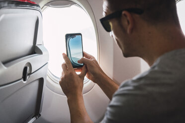 Man in airplane, using smartphone, taking a picture, airplane window - KKAF02463