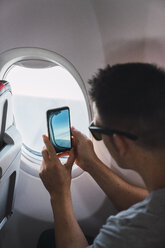 Man in airplane, using smartphone, taking a picture, airplane window - KKAF02464